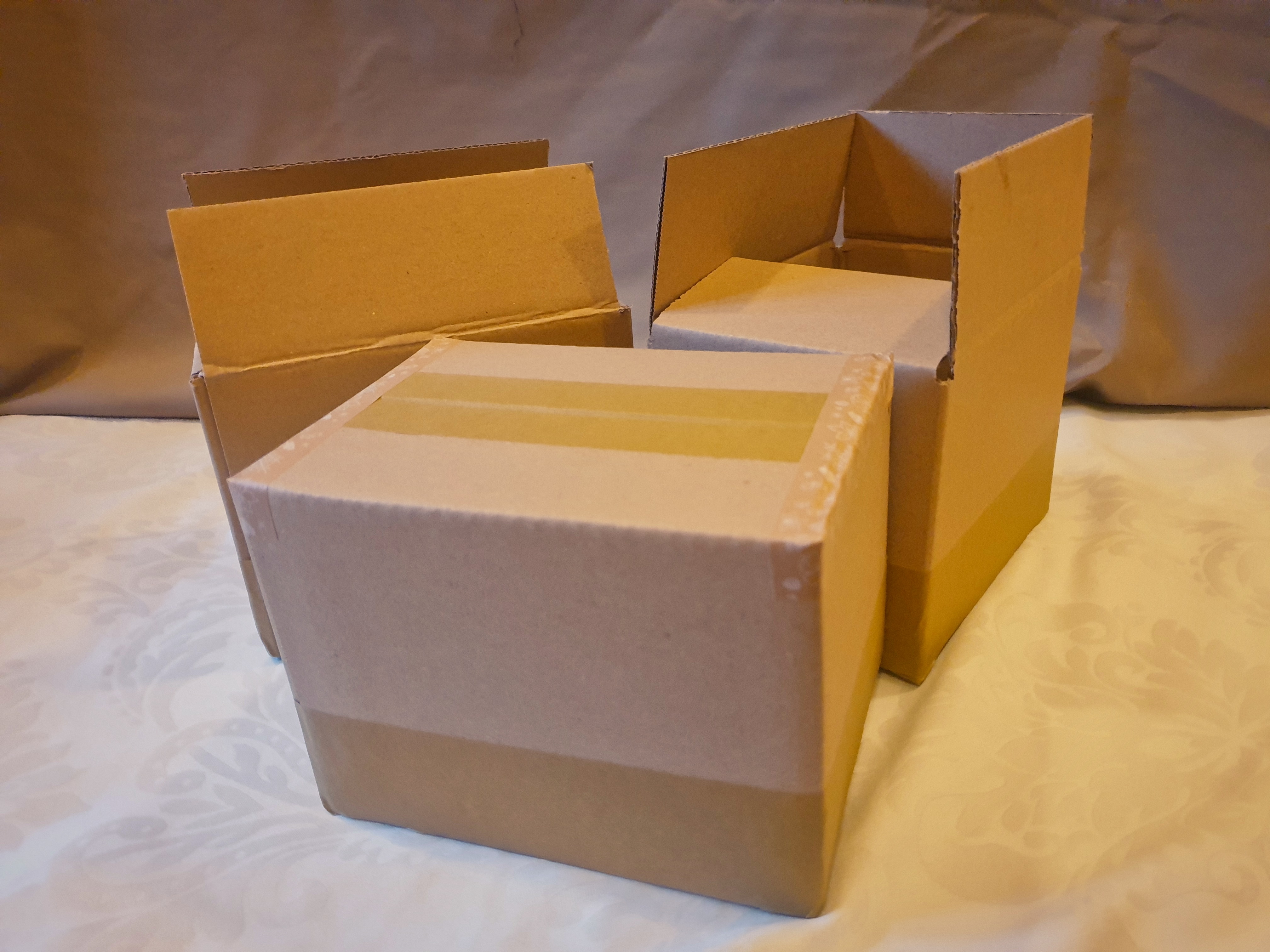 A photo of three cardboard boxes. The two in the background are opened, and the one in the foreground is packed.